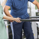Physiotherapist,Standing,By,Senior,Man,Walking,Between,Parallel