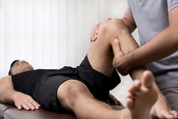 Therapist,Treating,Injured,Knee,Of,Athlete,Male,Patient,In,Clinic